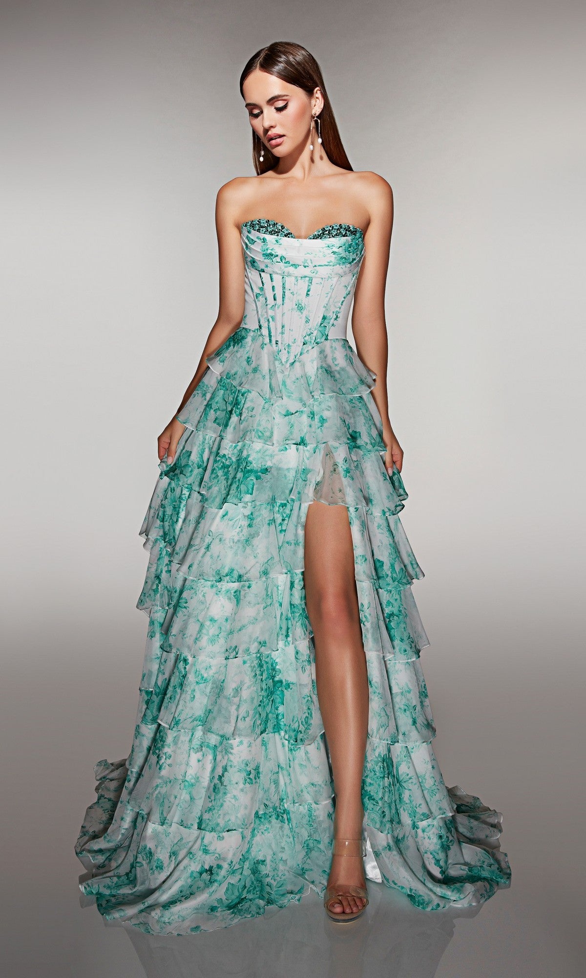 A woman in the Alyce 62192 long prom dress, featuring a strapless corset bodice and tiered Soft Jade/White floral chiffon ruffle skirt with a high slit, stands against a neutral background.